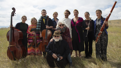 Peter & Cathy Halstead pose in front of an ensemble of musicians.