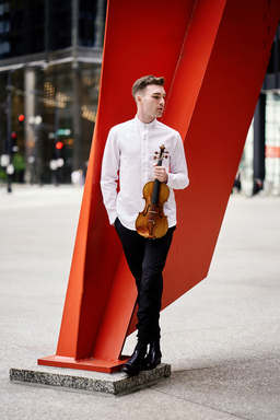Alexi Kenney holds his violin in front of a large bright red sculpture.