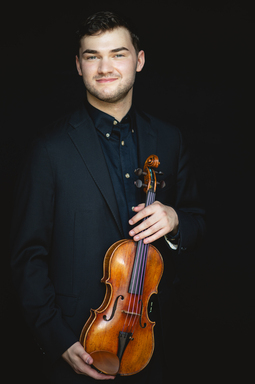 Nathan Meltzer holds his violin wearing a black suit.