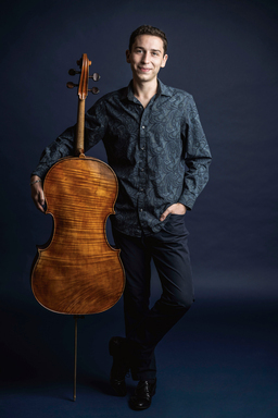 Oliver Herbert holds his cello showing the back of the instrument.