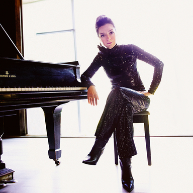 Yulianna Avdeeva sits a piano in a black pant suit with her legs crossed. 