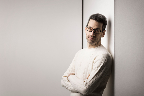 Jonathan Biss looks forward leaning against a white wall.