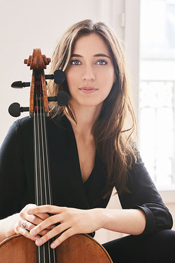 Camille Thomas stares into the camera while holding her cello by the neck.