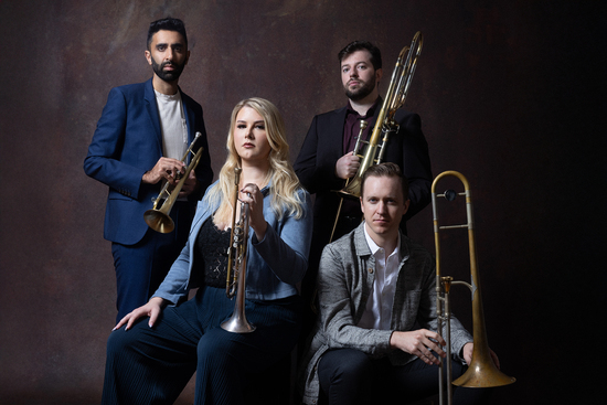 The Westerlies stand and sit as a group holding their trumpets and trombones.